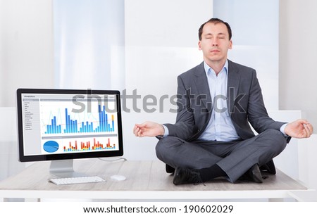 Full length of businessman mediating by computer on desk in office