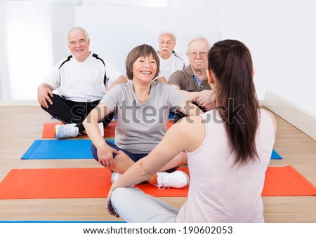Rear view of female trainer training senior customers on floor in yoga class