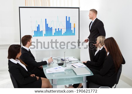 Businessman giving presentation on projector screen to colleagues in office
