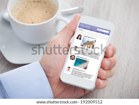 Cropped image of businessman surfing social networking site on mobilephone at office desk