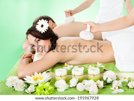 Portrait of smiling young couple receiving massage with herbal compress balls on back at beauty spa