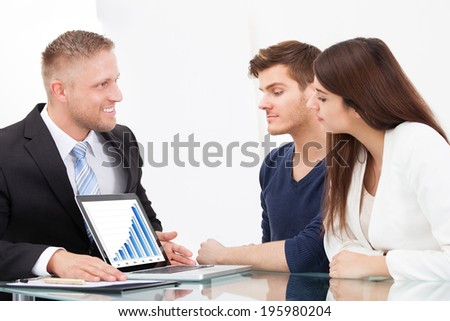 Male financial advisor showing investment plans to couple on laptop at office desk