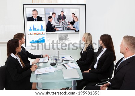 Businesspeople looking at projector screen in video conference meeting at office