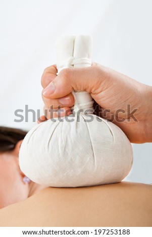 Closeup of young woman receiving massage with herbal compress bags on back at spa