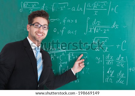 Portrait of confident young male professor standing against blackboard in classroom