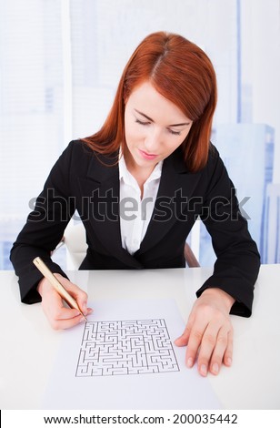 Young businesswoman solving puzzle on paper at desk in office