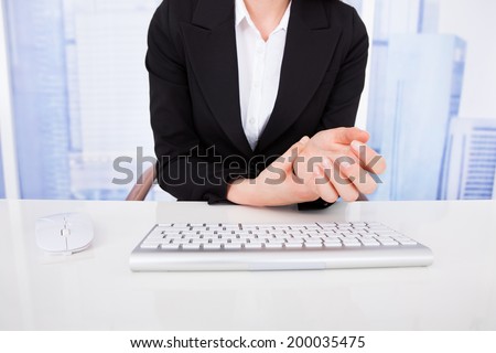 Cropped image of businesswoman suffering from wrist pain with computer keyboard on office desk