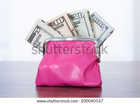 Variety of dollar bills in pink purse on table