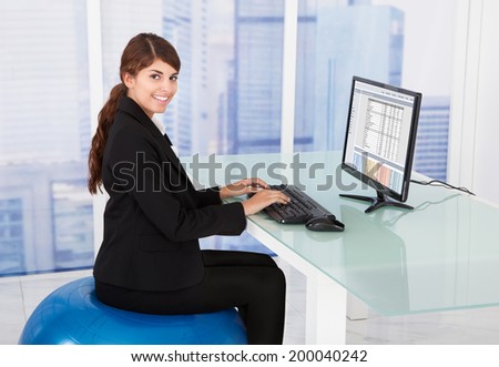 Side view of businesswoman using computer while sitting on fitness ball at desk in office