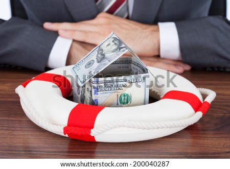 Midsection of businessman protecting money house with lifebuoy on table