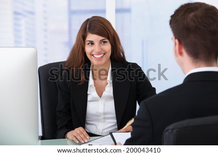 Happy young businesswoman interviewing male candidate at desk in office