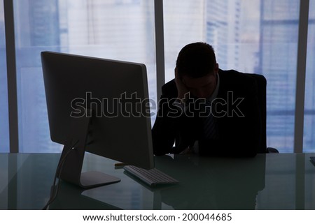 Stressed young businessman sitting at computer desk in office