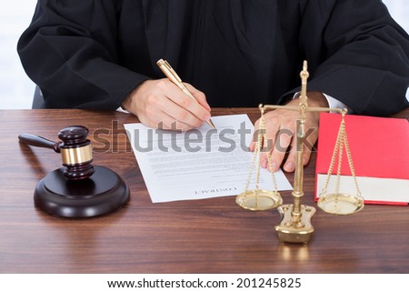 Midsection of male judge signing contract paper at desk