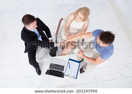 High angle view of young couple shaking hands with financial consultant in office