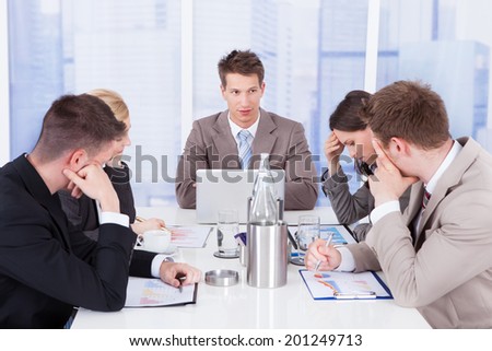 Young businessman looking at tired colleagues during conference meeting
