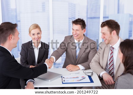 Two businessmen shaking hands in front of colleagues at office