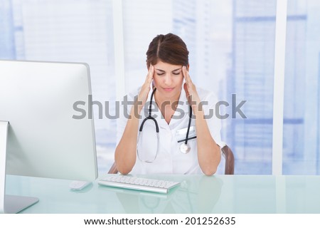 Sad female doctor with headache at computer desk in clinic