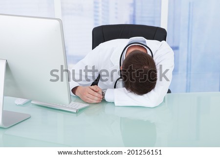 Tired young male doctor resting at computer desk in hospital