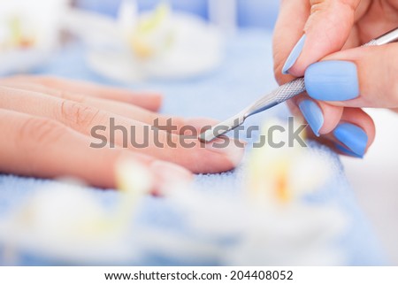 Cropped image of manicurist removing cuticle from the nail of woman at salon