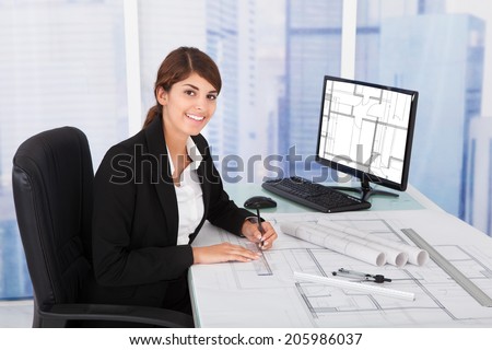 Young female architect working on blueprint at desk in office