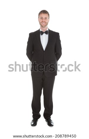 Full length portrait of confident waiter standing hands behind back over white background