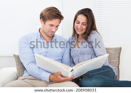 Happy couple looking at their photo album on sofa at home