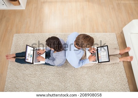 Full length of couple using laptops while sitting on rug in living room