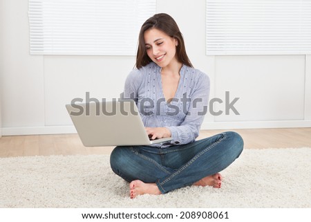 Full length of young woman using laptop while sitting on rug at home