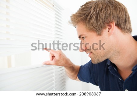 Side view of mid adult man peeking through blinds at home