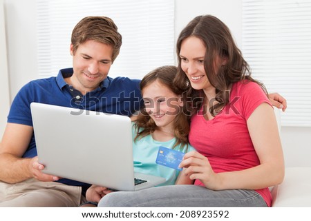 Happy family of three using laptop and credit card to shop online on sofa at home