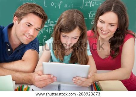 Smiling parents assisting daughter in using digital tablet while studying at home