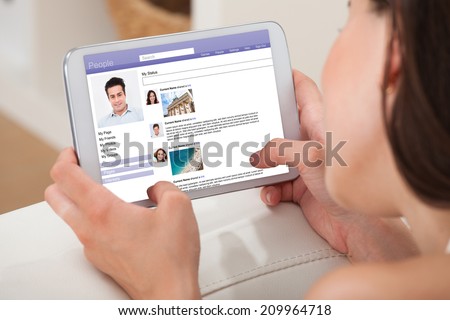 Cropped image of young woman using digital tablet to chat on social site while relaxing at home