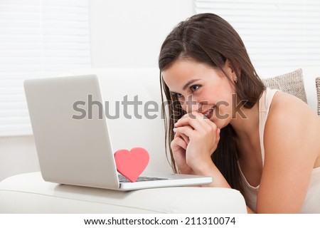 Side view of beautiful young woman dating online on laptop at home
