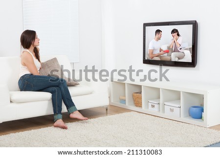 Full length of young woman watching television while sitting on sofa at home