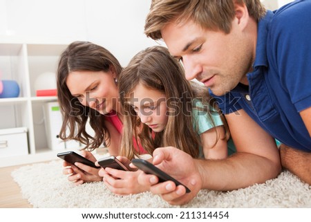 Family using smart phones while lying on rug at home