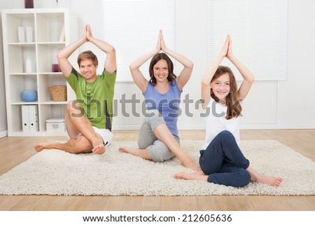 Full length portrait of smiling family practicing yoga on rug at home