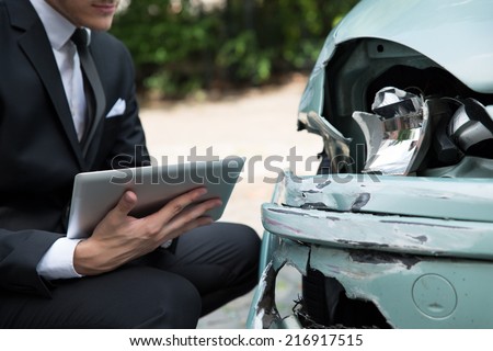 Side view of writing on clipboard while insurance agent examining car after accident