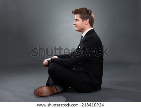 Side view portrait of smiling businessman sitting isolated over gray background