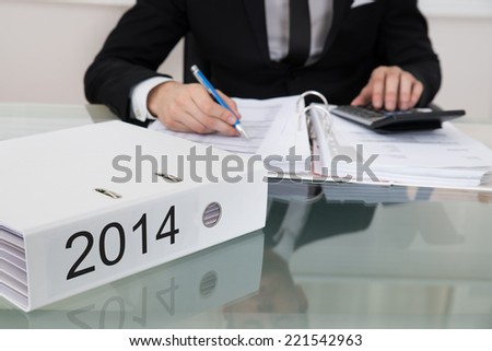 Midsection of businessman calculating taxes for 2014 at desk in office