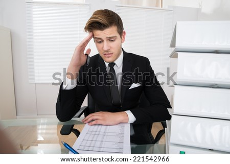 Worried young businessman reading document at desk in office