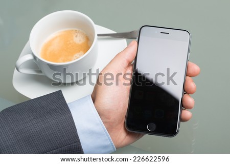 Berlin; Germany - October 10; 2014: Closeup of businessman holding Apple iPhone 6 at table. Apple iPhone 6 was launched on September 19; 2014