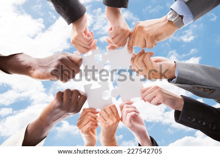 Directly below shot of multiethnic business people assembling jigsaw puzzle against sky