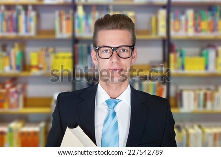 Portrait of confident male professor standing against bookshelf at college library