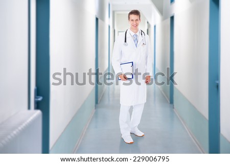 Full length portrait of confident doctor holding clipboard on corridor in hospital