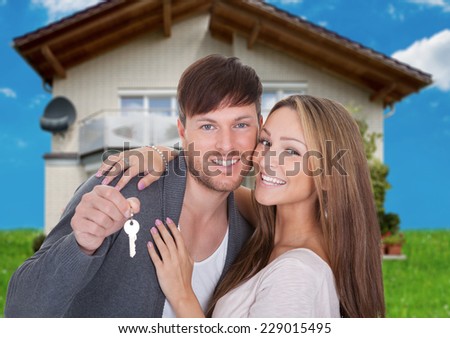 Portrait of happy young couple with key against new home