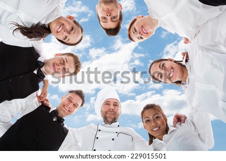 Directly below portrait of happy chef and waiters standing in huddle against sky