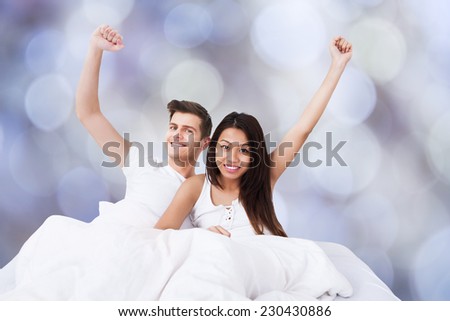 Portrait of successful multiethnic couple with arms raised on bed