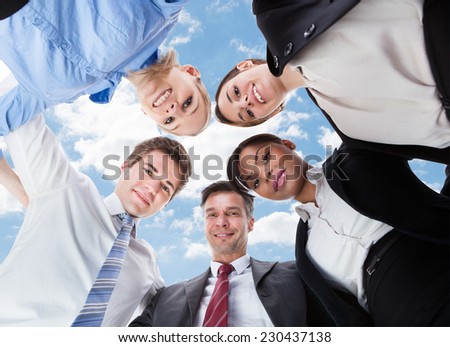 Low angle portrait of multiethnic business people forming huddle against sky