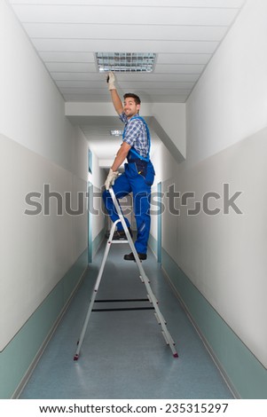 Full length portrait of electrician on stepladder installs lighting to the ceiling in office