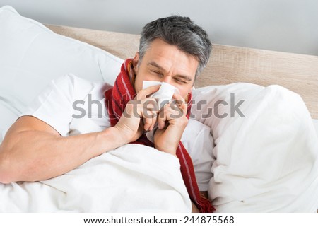Sick Mature Man Blowing His Nose While Lying On Bed At Home